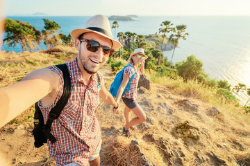 Wall Mural - We love traveling and trekking! Adventure Selfie. Caucasian young loving couple taking selfie while they walking on mountains near the sea.