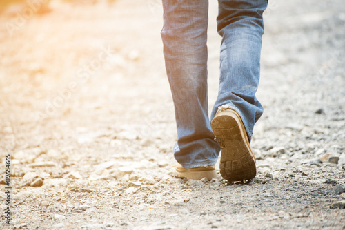 Fotografía Lonely man wearing jeans and leather boots walking along the path strewn with rocks