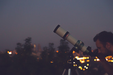 Wall Mural - man looking at the stars with telescope with de-focused city lights.