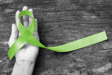 Wall Mural - Lymphoma Cancer Awareness Lime Green color ribbon w/ helping hand on old aged wood background: Satin fabric loop symbolic logo raising support help people life living w/ tumor illnesss