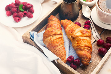 Wall Mural - Morning breakfast in bed with cup of coffee, croissants, fresh berries and honey on wooden tray, selective focus