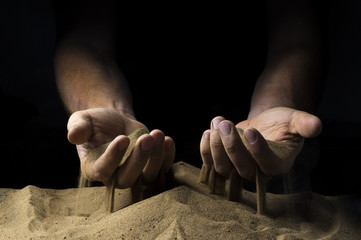 Wall Mural - pours sand from his hands on a black background