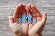 Paper family in hands on wooden background welfare concept