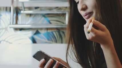Young girl sitting in bathroom using smartphone. Smoking electronic cigarette. Steam
