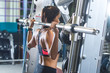 Fit woman doing shoulder press exercise with a weight bar Smith machine at gym.