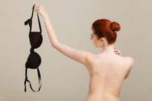 Naked woman holds black bra in hand