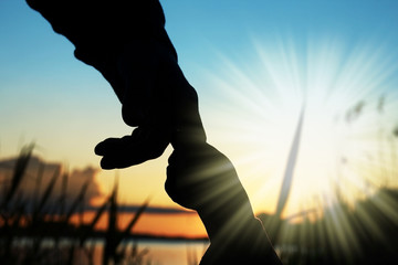 silhouette of hands of parent and child at sunset