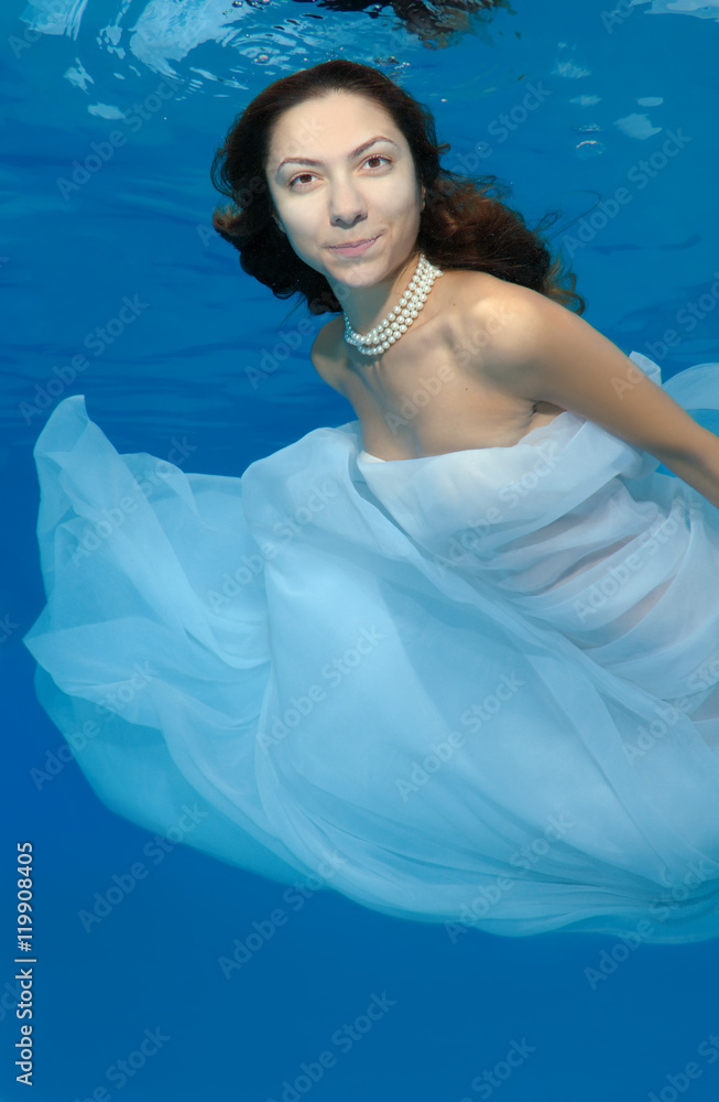 Young beautiful woman with long hair in a long white dress under water ...