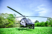 Black With Gray Stripes Helicopter Standing On Green Grass Field Getting Ready To Fly Over Blue Sky.