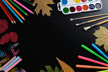 Wall Mural - The composition of the white paper, color paint, brushes, pens, pencils, paper clips, autumn leaves on a background of black school board