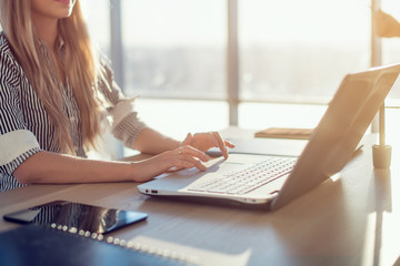 Woman blogging in spacious office using computer on her workplace. Female employee sitting, smiling, looking at camera.