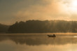 Człowiek wędkujący na łódce mglisty, złoty poranek.