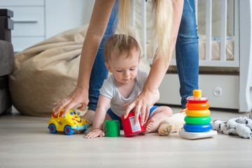 mother giving toys to her 10 months old baby boy playing on floo