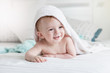 Adorable smiling baby in hooded towel ling on bed after having b