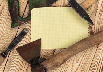 Old carpentry tools and a piece of notebook on a wooden backgrou