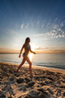 © johnqsbf - attractive sexy woman in bikini walking on sand on lonely beach on sunset sunrise