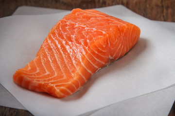 One piece of fresh salmon on white baking paper. Dark wood backg