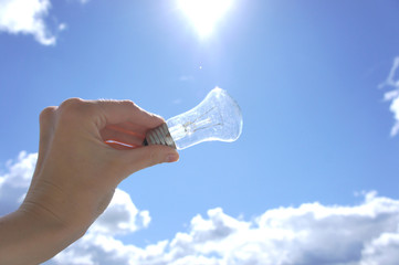  Hand holding light bulb on a background sky and sun. An abstract idea on the topic of electricity of solar energy.  
