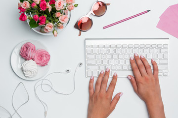 Office desk table with female hands, computer, supplies, flowers