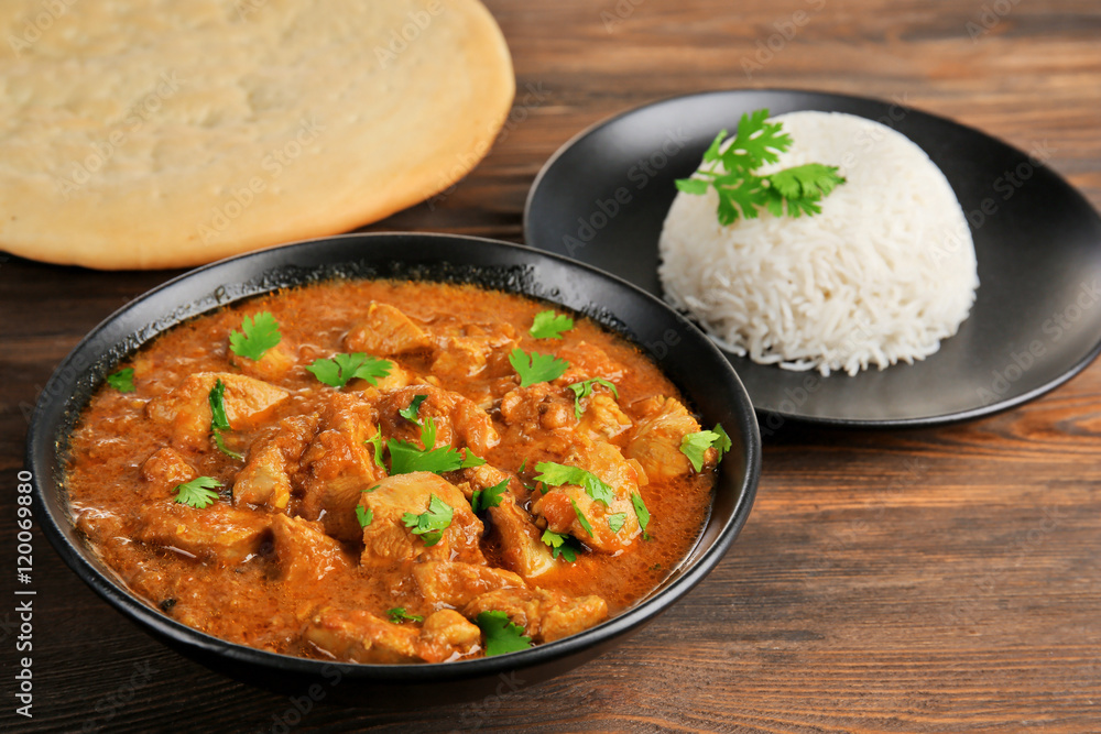 Tasty dinner with chicken curry in bowl on wooden background