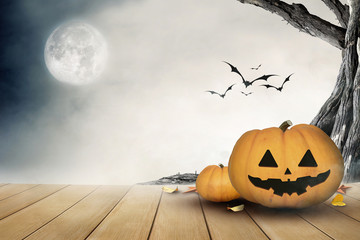 halloween pumpkin in a dark mist forest at night and wooden table, over light 