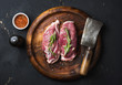 Raw uncooked poultry meat cut. Duck breast with rosemary, spices and butcher cleaver on dark wooden tray over black wooden background, top view