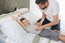 Father Tickling His Son On The Bed