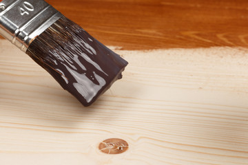 Brush on can of brown paint on partly painted wood, close up, lo