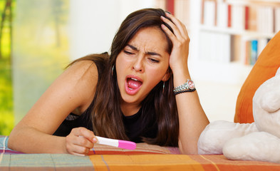 Wall Mural - Pretty young brunette woman lying down holding pregnancy home test, staring at it in disbelief, looking emotional, garden window background