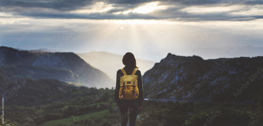 Hipster young girl with backpack enjoying sunset on peak mountain. Tourist traveler on background valley landscape view mockup. Hiker looking sunlight flare in trip in Spain basque country Europa - obrazy, fototapety, plakaty 