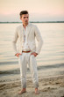 © ronedya - young handsome man in a white suit near the sea at sunset. young handsome groom on the beach. Close-up