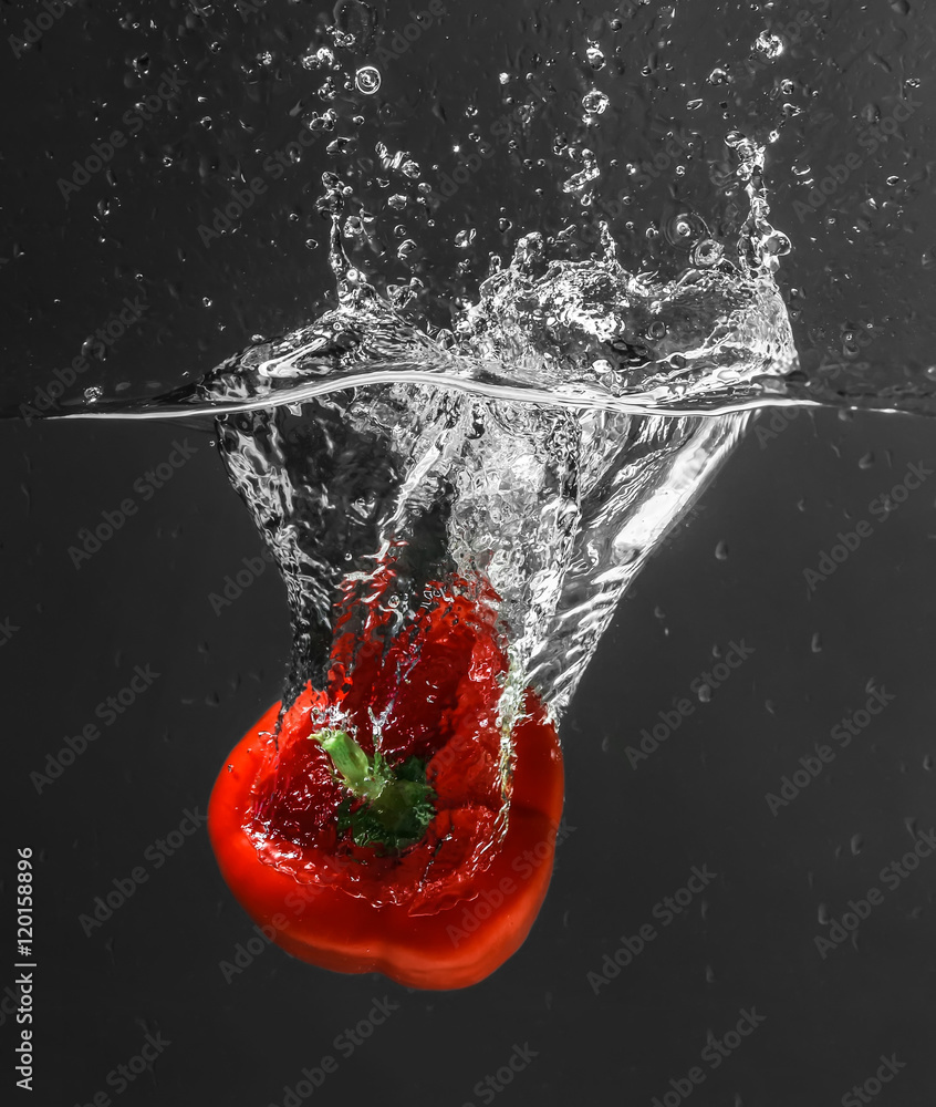 Fresh red bell pepper falling in water on dark background