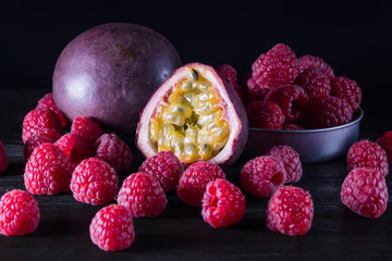 Passionfruit and many raspberries on black wooden table on dark