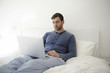 © Picxel Creative - Man using a laptop while relaxing on the bed