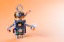 Robot Concept Retro Style. Circuits Socket Chip Toy Mechanism, Funny Head, Eyes Glasses, Light Bulbs In Hands. Copy Space, Orange Background