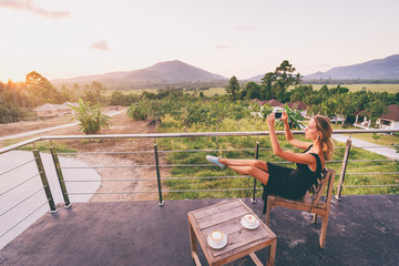 Relax and technology. Pretty young woman taking picture on smartphone camera while sitting on cafe terrace with beautiful mountains view.