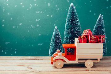 Wall Mural - Christmas toy truck with gift boxes and pine tree on wooden table over green background