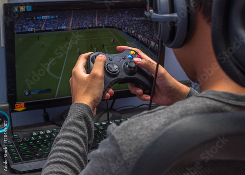 Fotografía Back view of young gamer playing video game wearing headphone using his controller