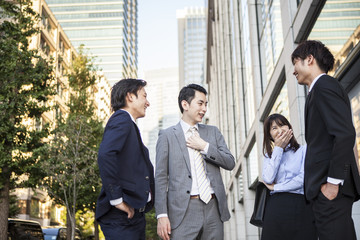 Canvas Print - Four businessmen who are the stand talking in front of the office building