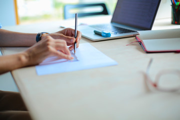 Young woman sitting at the desk with instruments, plan and laptop