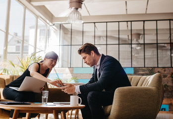 Wall Mural - Two people sitting in office lobby using mobile phone