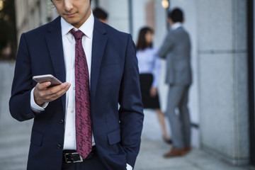 Canvas Print - Businessman, looking at a smart phone in the office district