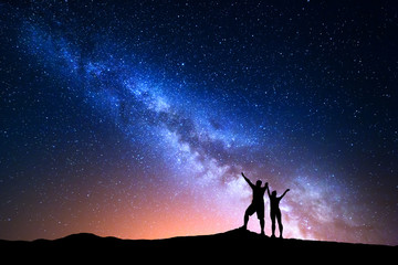 milky way. colorful night sky with stars and silhouette of standing happy man and woman with raised 