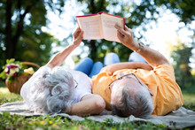 Senior Couple Resting At Park, Reading A Book
