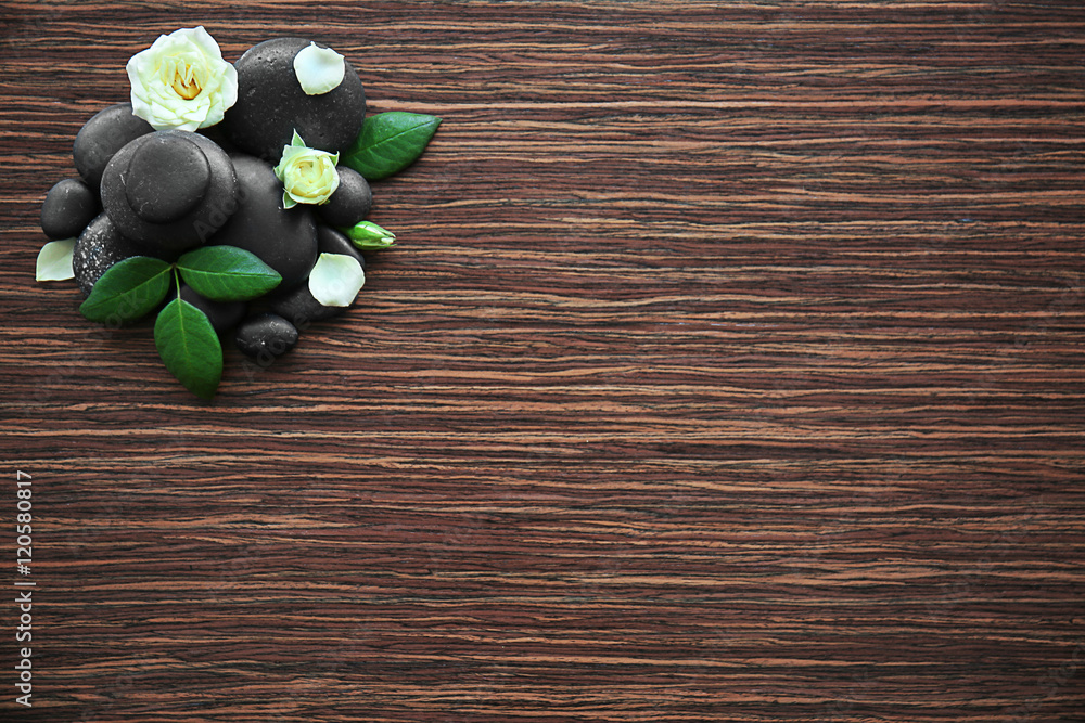 Spa stones with rose and petals on wooden background