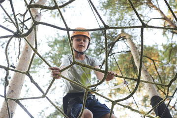 Portrait of active brave boy enjoying outbound climbing at adventure park on tree top