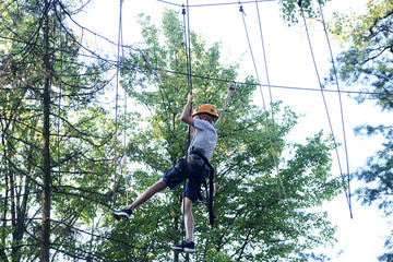 Portrait of active brave boy enjoying outbound climbing at adventure park on tree top