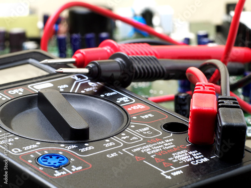 Fotografía multimeter closeup with probes and circuit board in background, shallow depth of