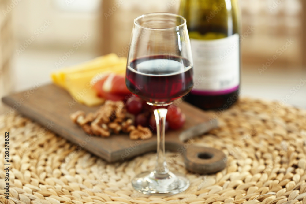 Glass with red wine and tasty snacks on a board on wicker mat