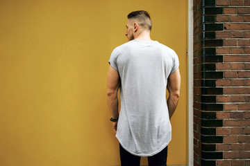 Attractive young muscular man wearing a gray T-shirt standing on a background of yellow wall. back view. empty place for your logo o design. mock-up of blank t-shirt.